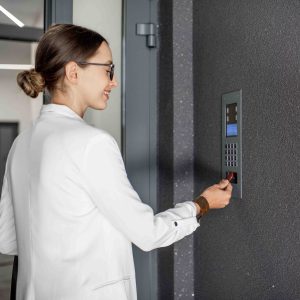 Young business woman in white suit touching the intercom with keychain opening the door of residential modern building